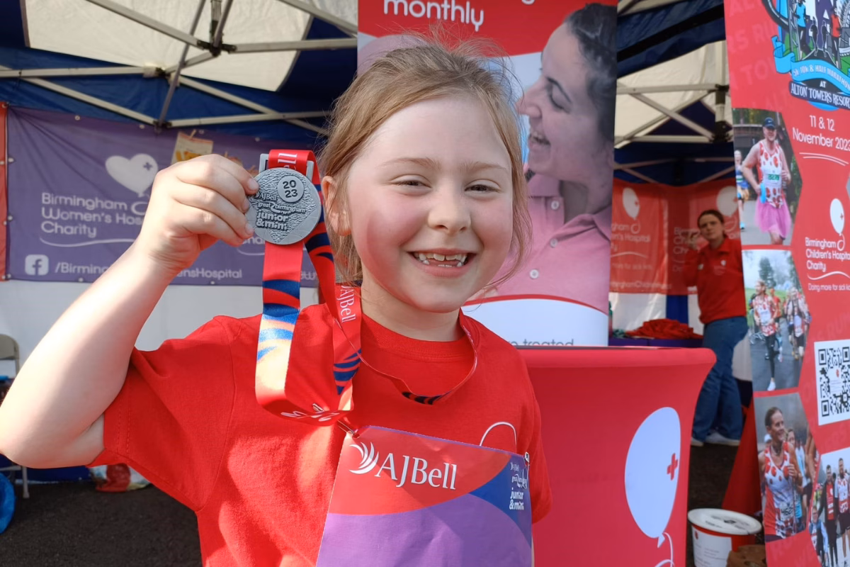 Florence holding her run medal and smiling, wearing a red charity t shirt