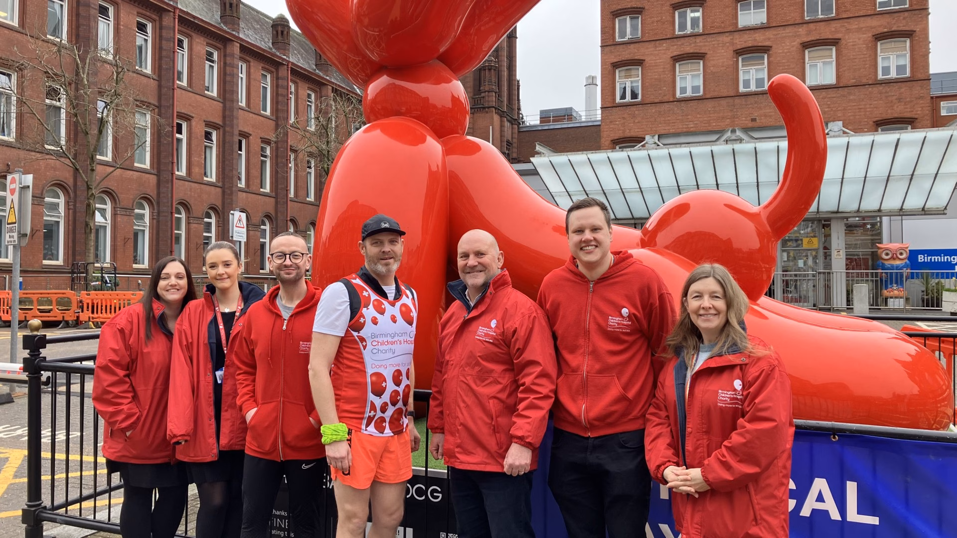 A group of people dressed in red clothes stand in front of a red statue.
