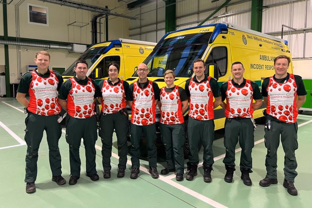 Paramedics standing in row in front of ambulances, wearing red charity running tops.