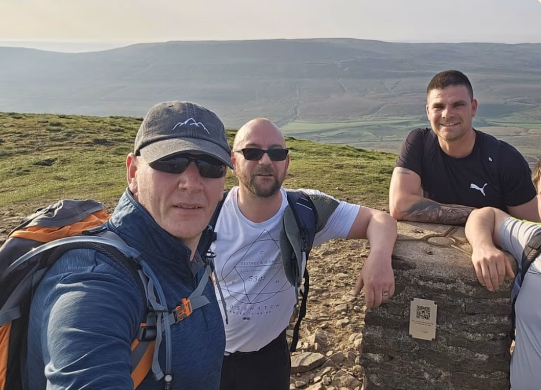 Three men pose for a photo at the top of a mountain