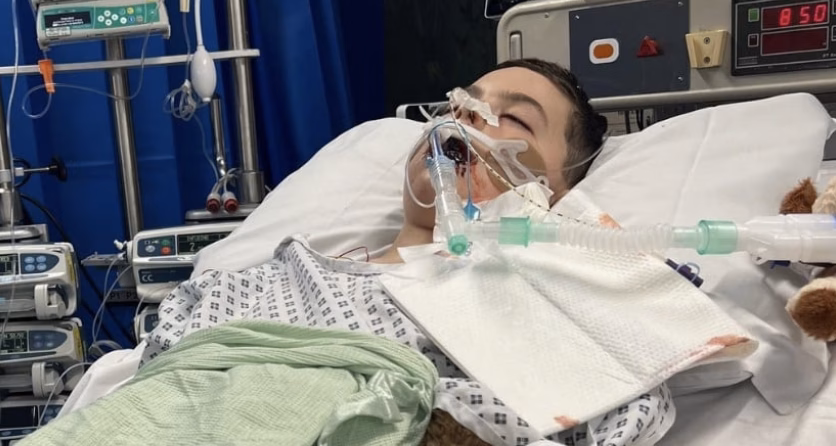 A young boy in a hospital bed with tubes and medical equipment around his face