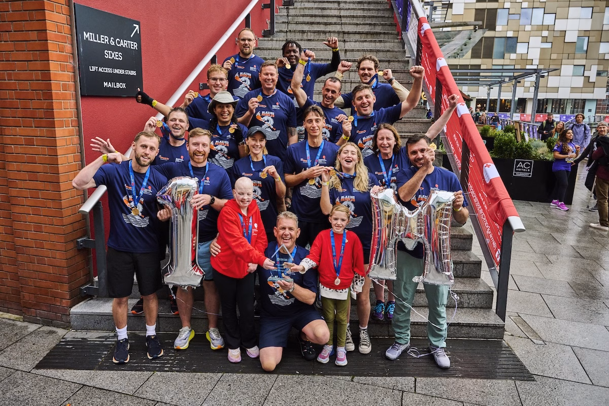 Dragon Boat Race winners sat on the steps at the Mailbox Birmingham with patients holding up '£1m' balloons