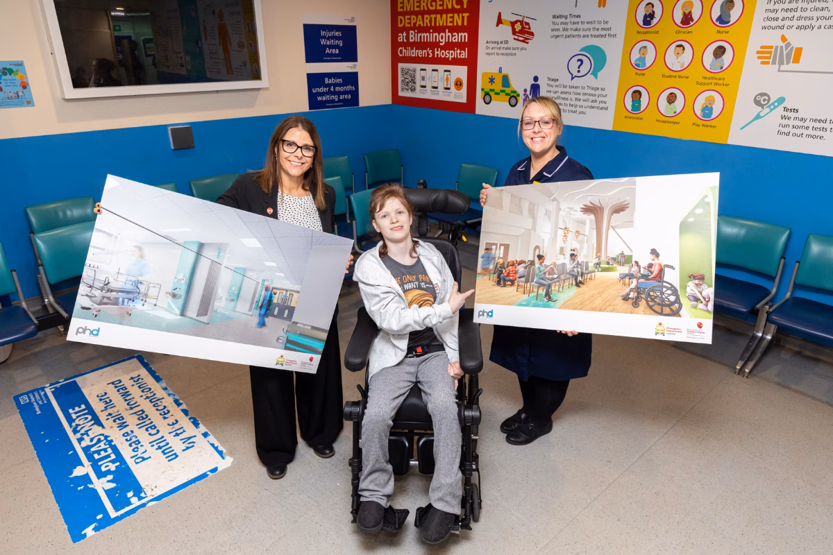 Patient Bella Cox with Katie Johnston and Miranda Williams, holding CGI images of transformed ED Department
