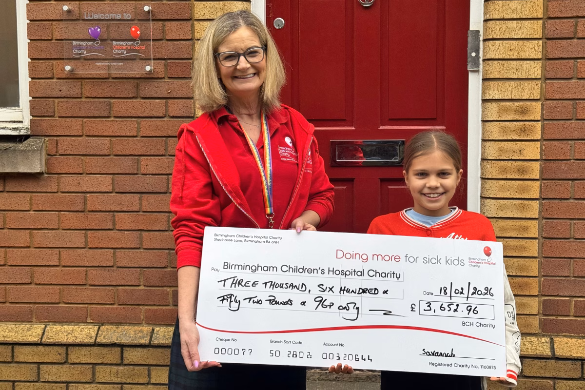 Amanda Delvin (left) and Savannah Cox (right) smiling and holding up fundraising cheque outside charity offices