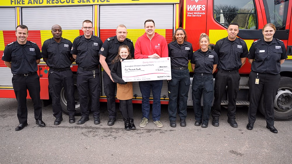 Simon and the Ward End Fire Station crew standing in front of fire engine with fundraising cheque