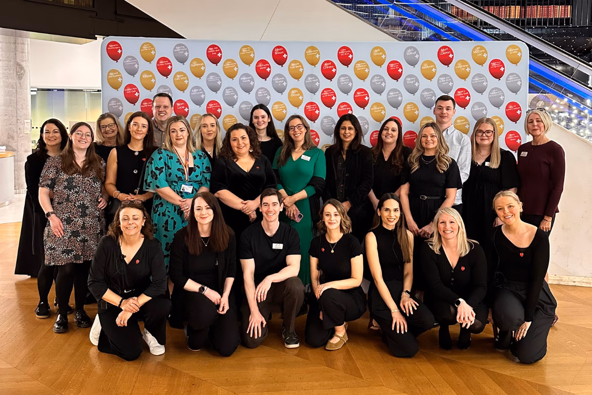 Smiling group of charity staff in front of balloon banner at 100 Heroes event