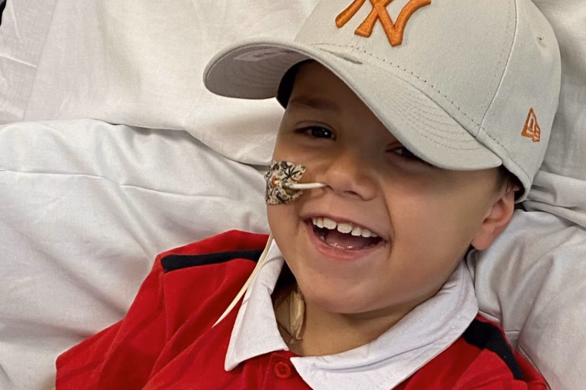 Smiling boy wearing a cap and a red Manchester United football shirt with a nasal tube