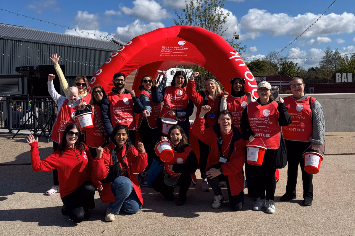 Group of charity staff under inflatable arch holding collection buckets and celebrating