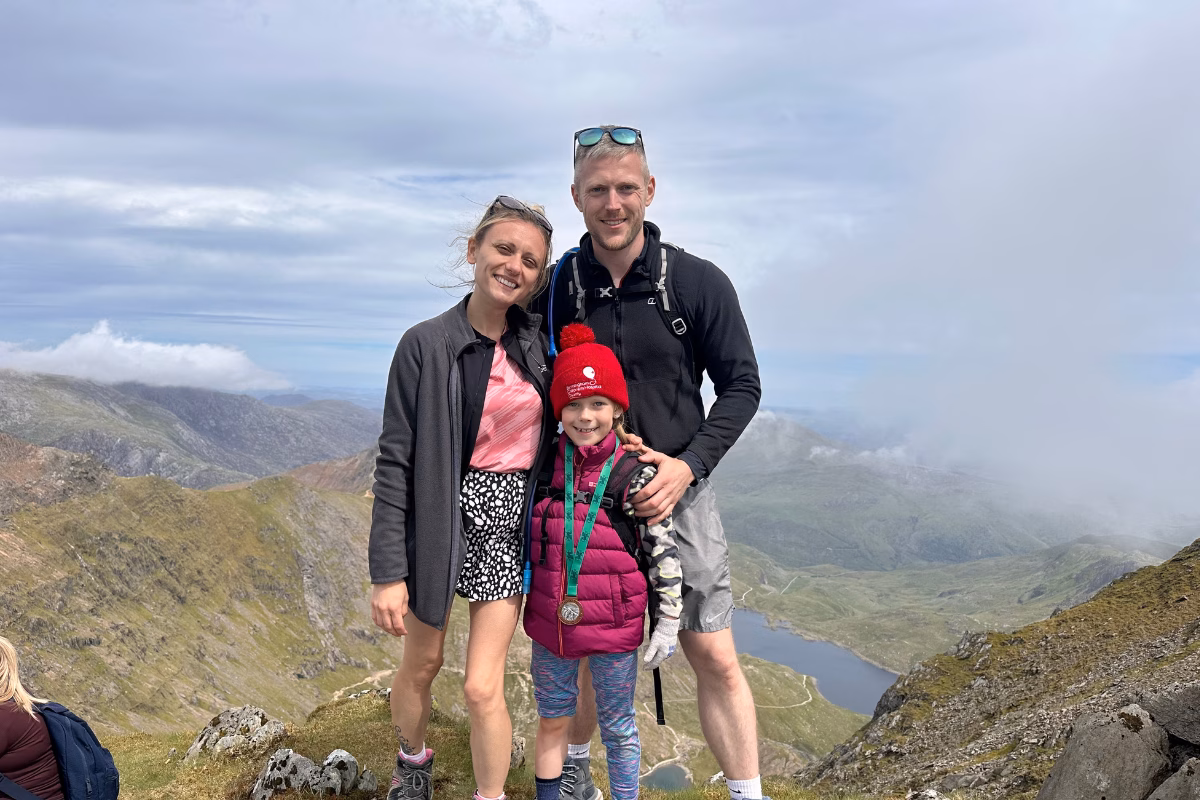 Man and woman with girl in hiking gear standing on top of a mountain