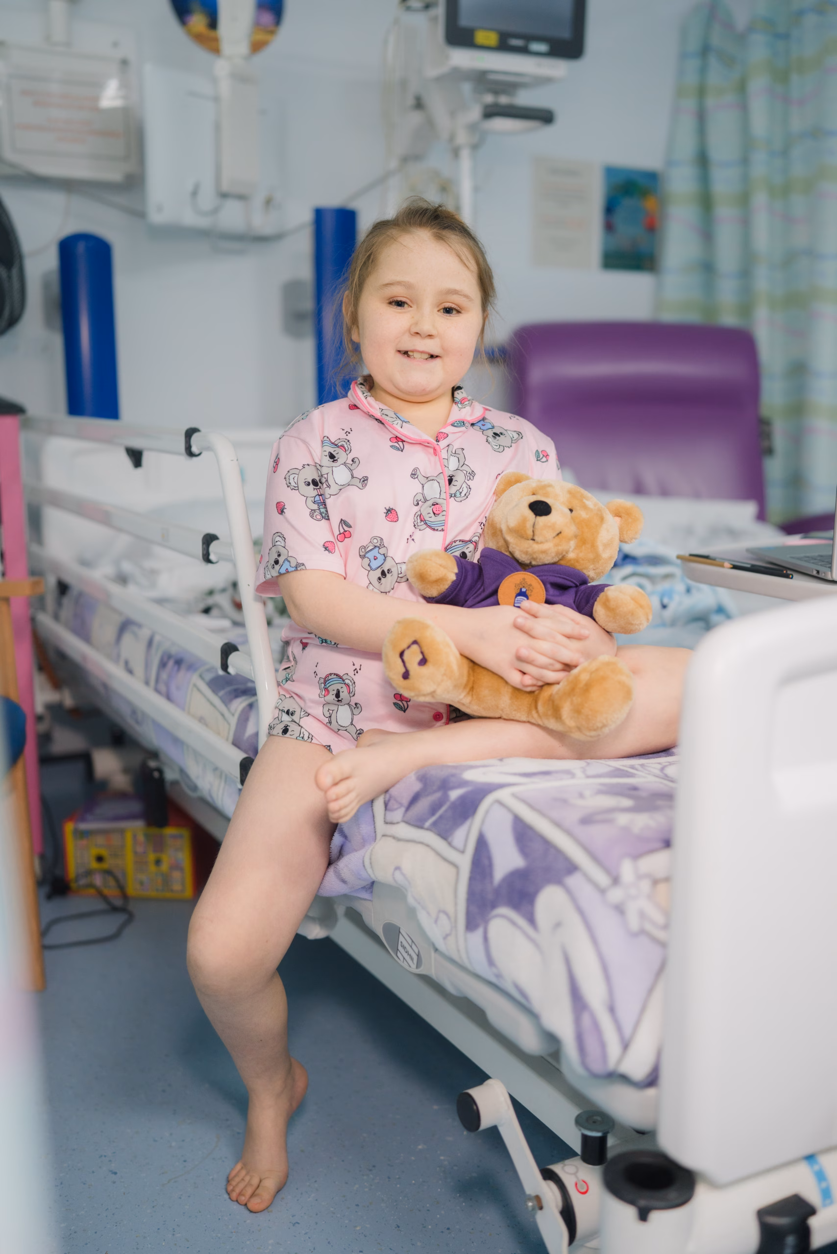 young girl holding a teddy bear in hospital bed