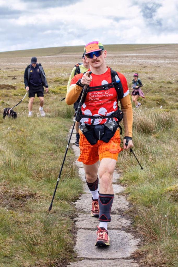 Man in red BCH top hiking on hillside with walking poles