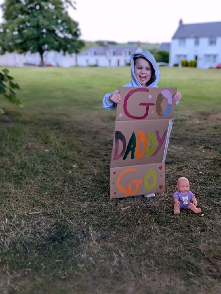 Harper standing outside with cardboard sign saying Go Daddy!