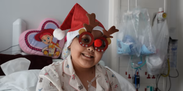 Young patient, wearing Christmas hat and glasses, smiling at the camera