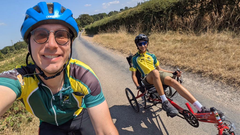 Adult in cycle helment next to student in cycle helmet on adapted bike