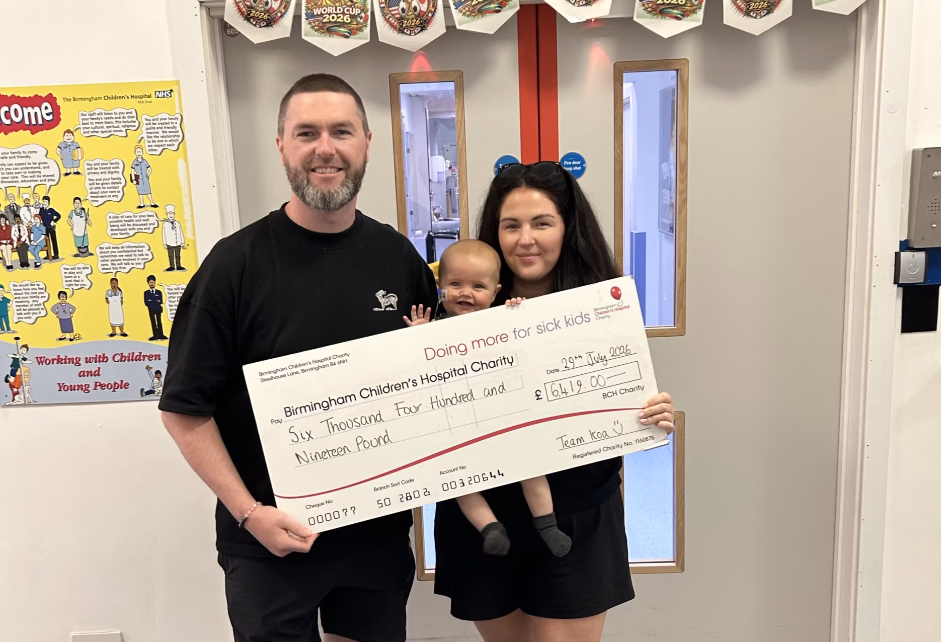 Man, woman and baby holding up giant fundraising cheque