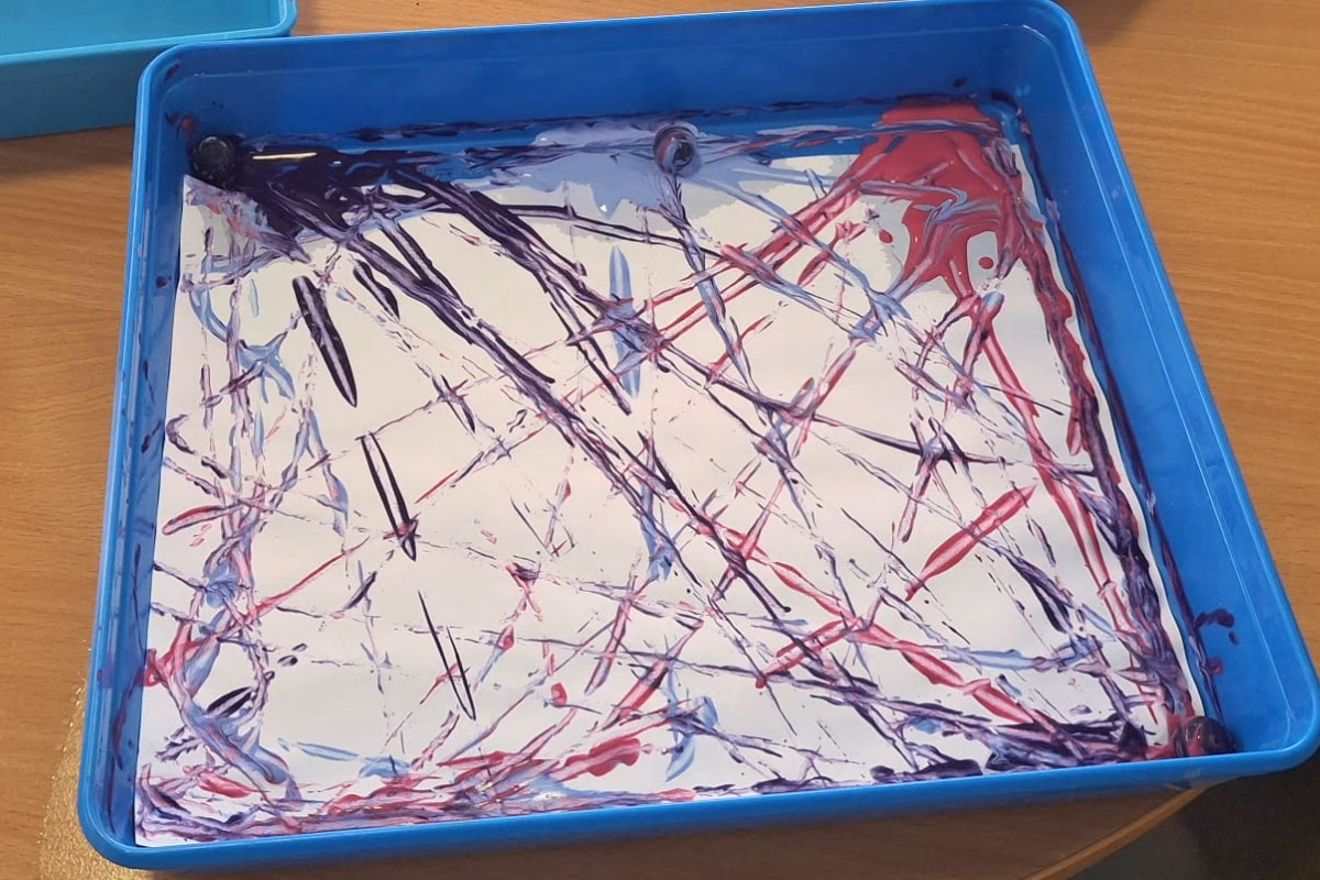 Tray with paint streaked paper and a marble