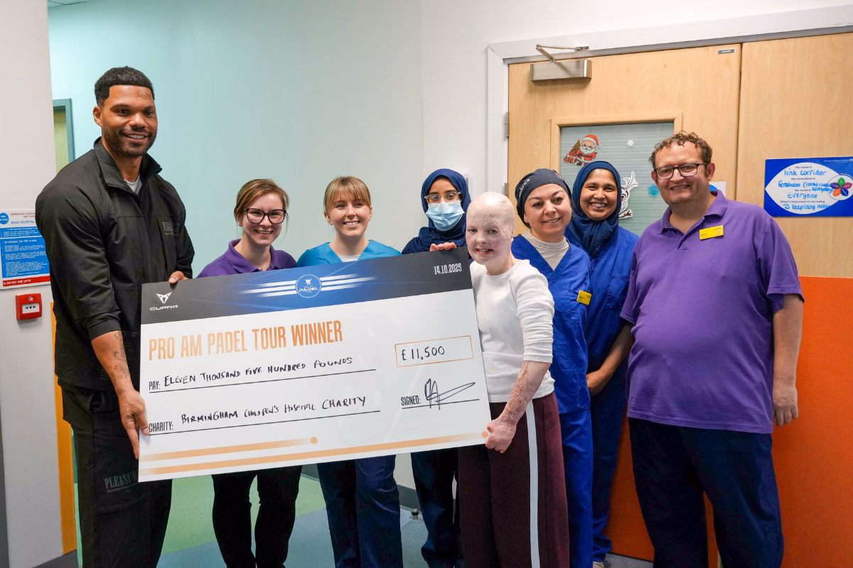Joleon Lescott and patient Elizabeth Soffe holding fundraising cheque with Burns Centre staff in hospital corridor