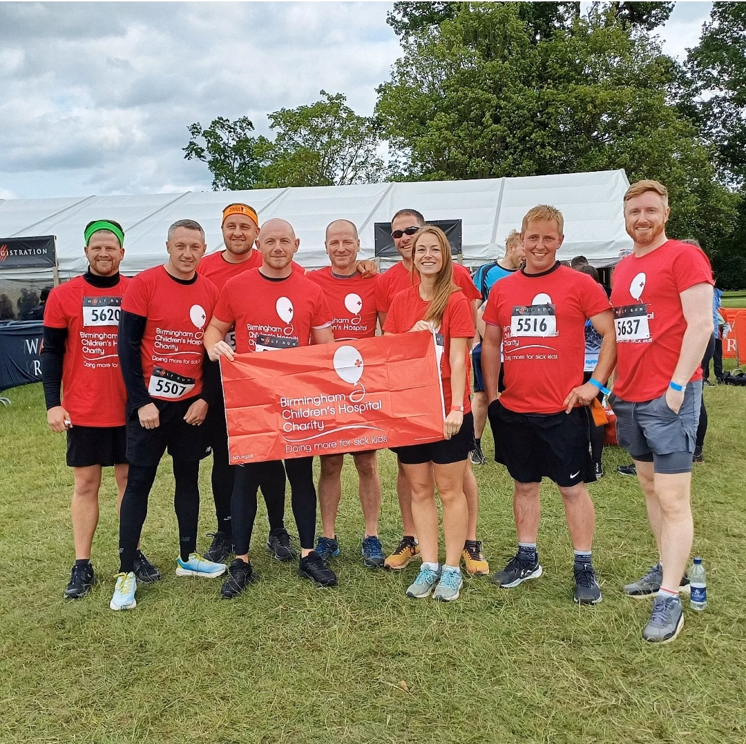 Group of staff wearing red t shirts outdoors in field holding BCH charity banner