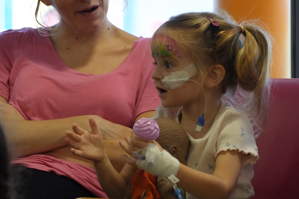 Girl with bandage on arm and rainbow facepaint clapping