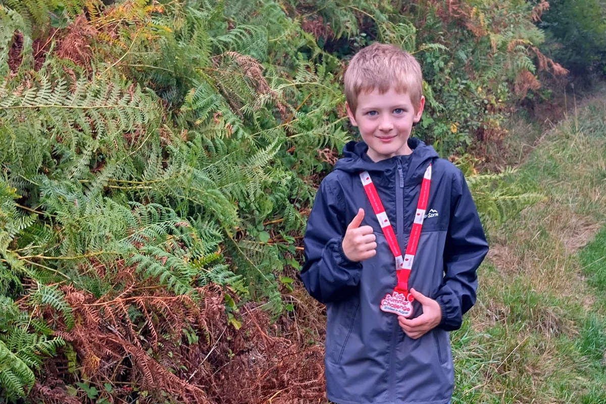 Child with red medal on lanyard doing thumbs up in park
