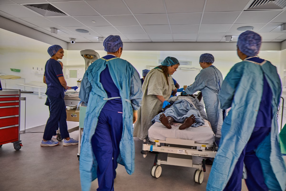 Clinicians in surgical gear around a hospital bed simulating birth care with a mannequin